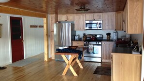 A kitchen with wooden cabinets, stainless steel appliances, a red door, and a wooden table with a checkered tablecloth. - Vermont lake house,Vermont get away, come and relax (Elmore)