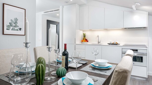 A modern dining area with a table set for four, white cabinets, a kitchen with a fruit bowl, and a framed plant on the wall. - Merced IV - Penthouse apartment in Malaga (Málaga)