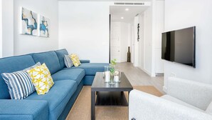 A modern living room with a blue sofa, a grey armchair, a coffee table, and a flat-screen TV mounted on the wall. - Merced IV - Penthouse apartment in Malaga (Málaga)