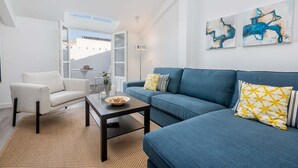 A modern living room with a sofa, armchair, and coffee table. There is a window with a view of buildings outside. - Merced IV - Penthouse apartment in Malaga (Málaga)