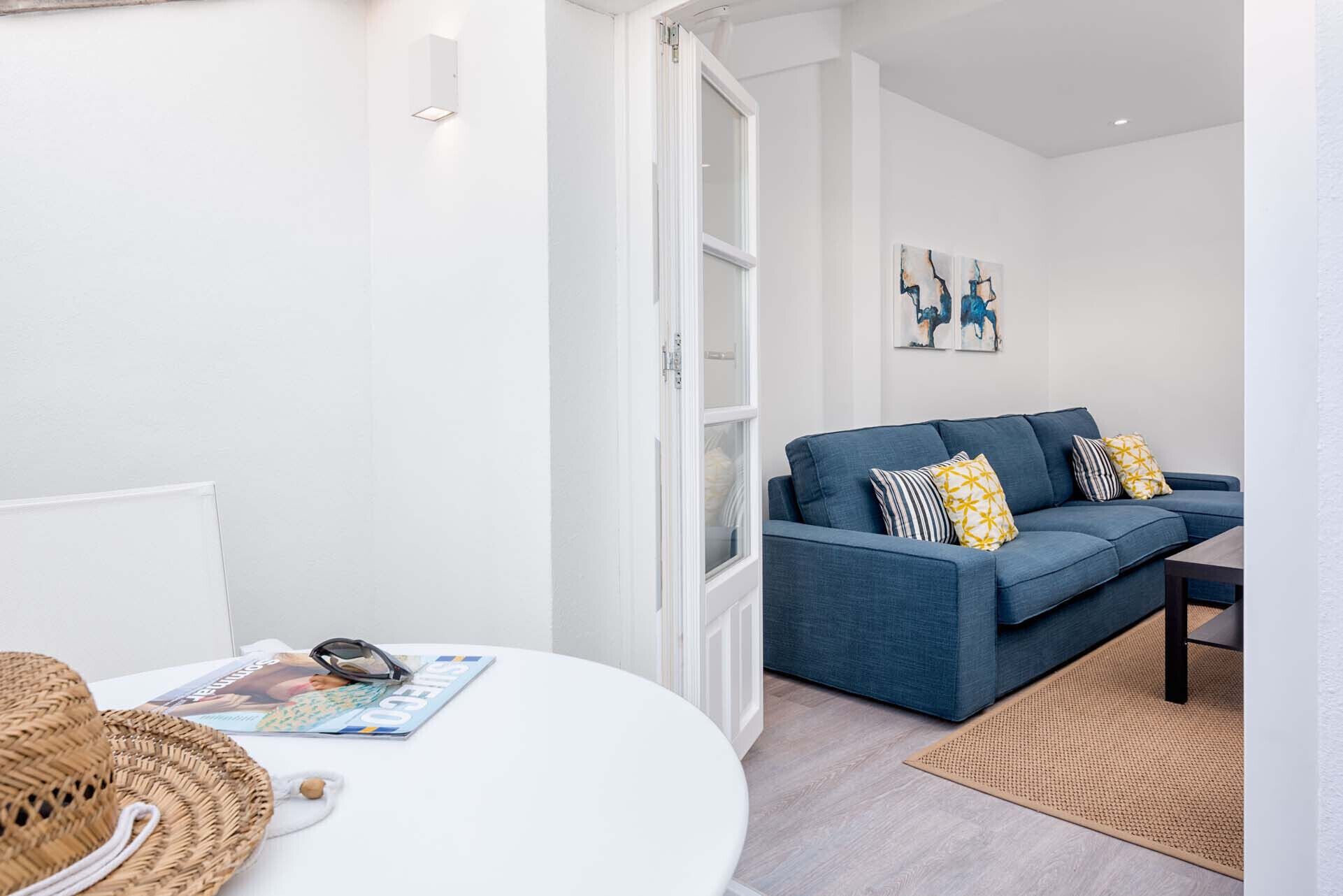 Un salón moderno con un sofá azul, paredes blancas y una revista sobre una mesa.