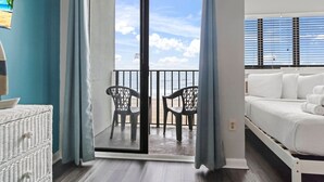 A balcony with a view of the beach, a white bed, and a wicker chair. - Palace 202 (Myrtle Beach)