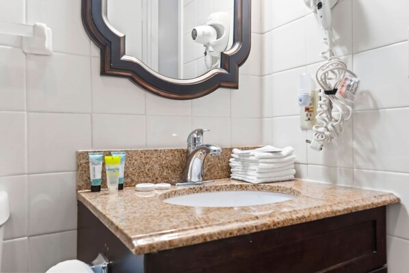A bathroom with a granite countertop sink, a mirror with a decorative frame, a hairdryer, and a towel rack.