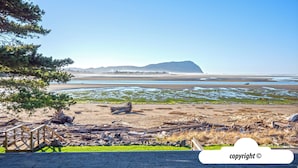 Un paisaje costero con un puente de madera, playa arenosa y montañas a lo lejos.