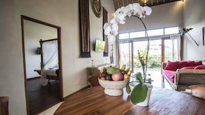 A wooden dining table with a fruit bowl, a potted plant, and a red couch in the background. - Junjungan Serenity Privite Villa, Spa & Pool (Ubud)