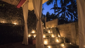A stone wall with a stone bench and a thatched roof structure. - Junjungan Serenity Privite Villa, Spa & Pool (Ubud)