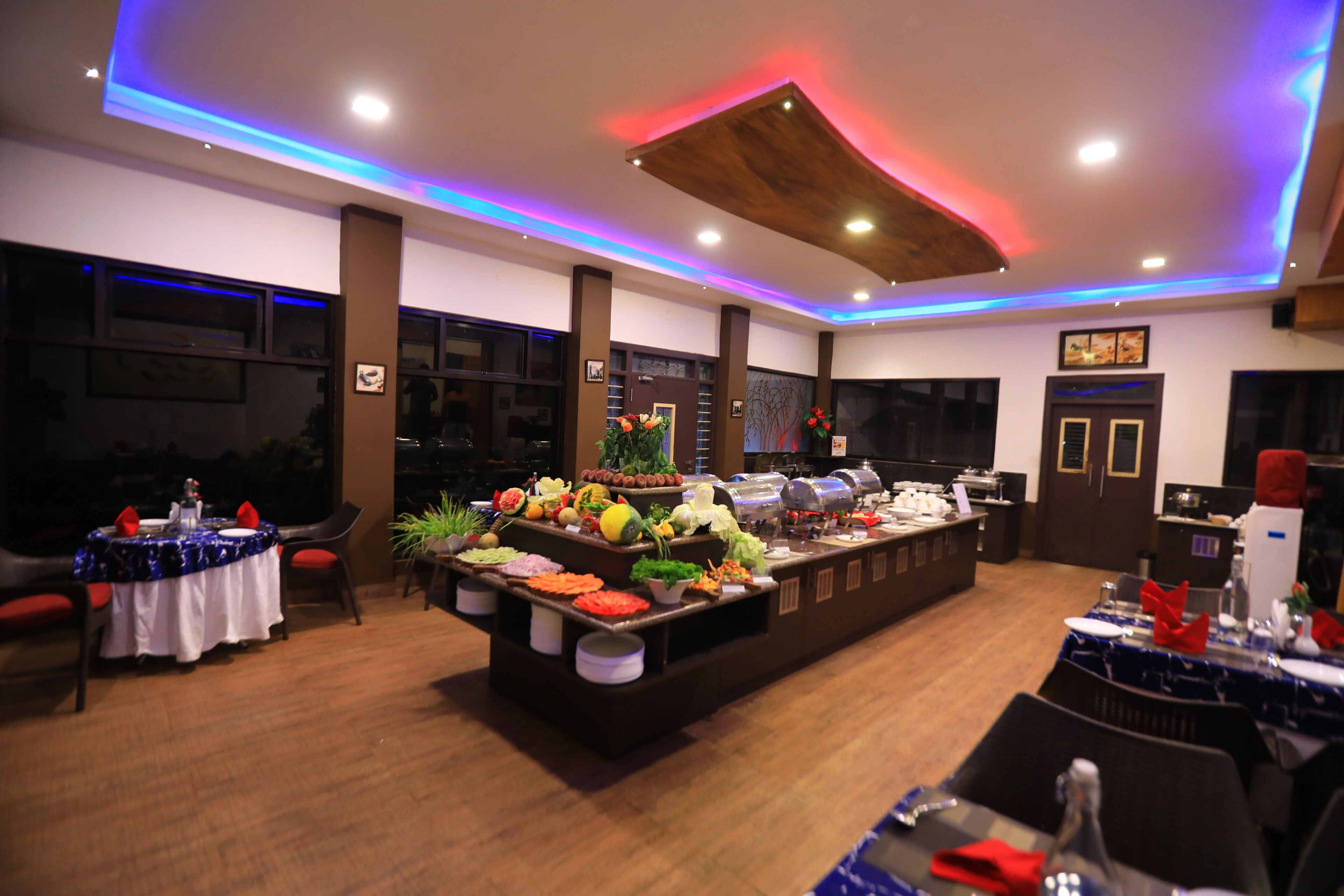 A buffet setup with various food items and a modern ceiling design with blue and red lighting.