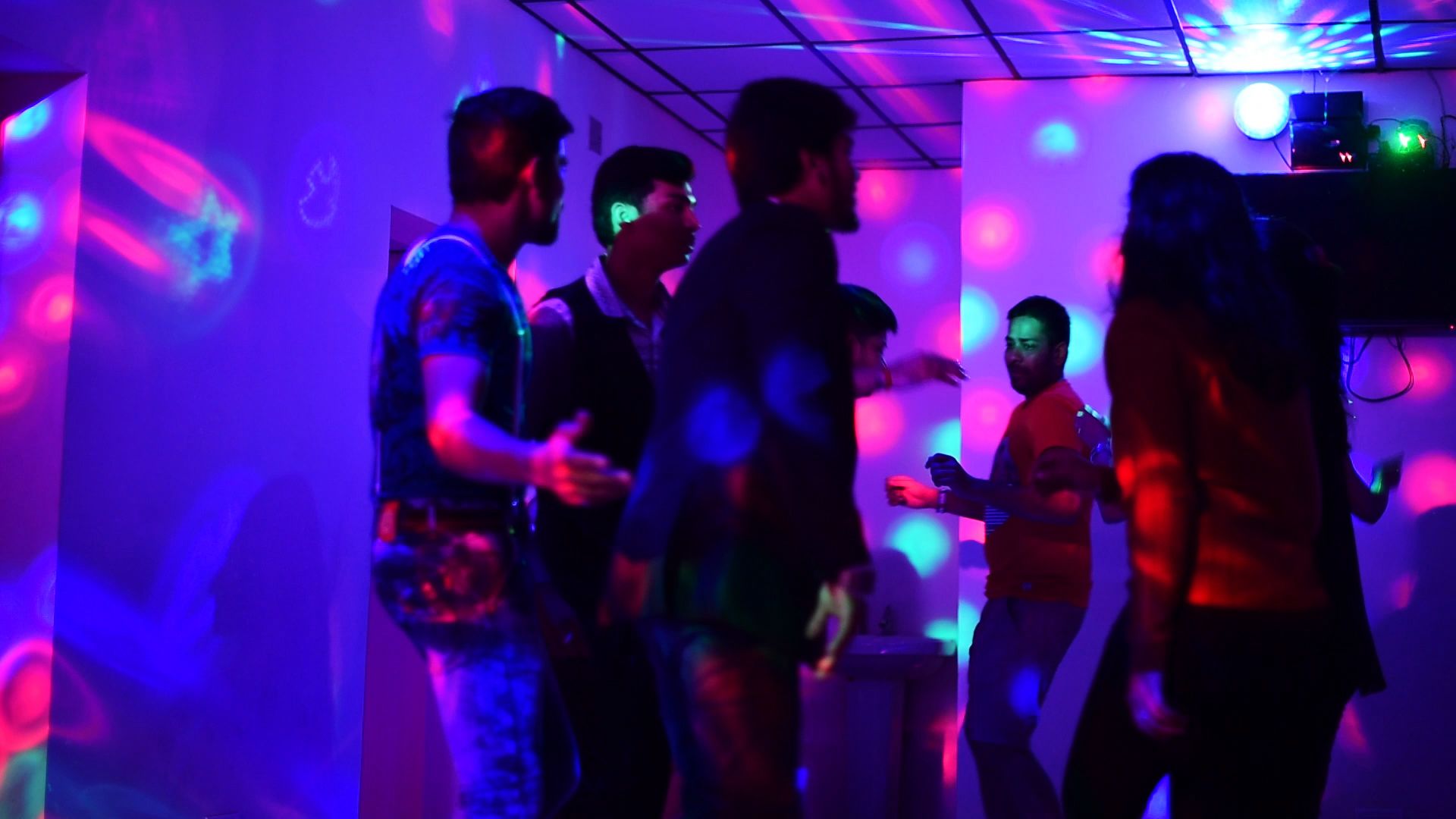 Un groupe de personnes qui dansent dans une pièce où l’on peut voir une structure de plafond et une installation pour DJ.