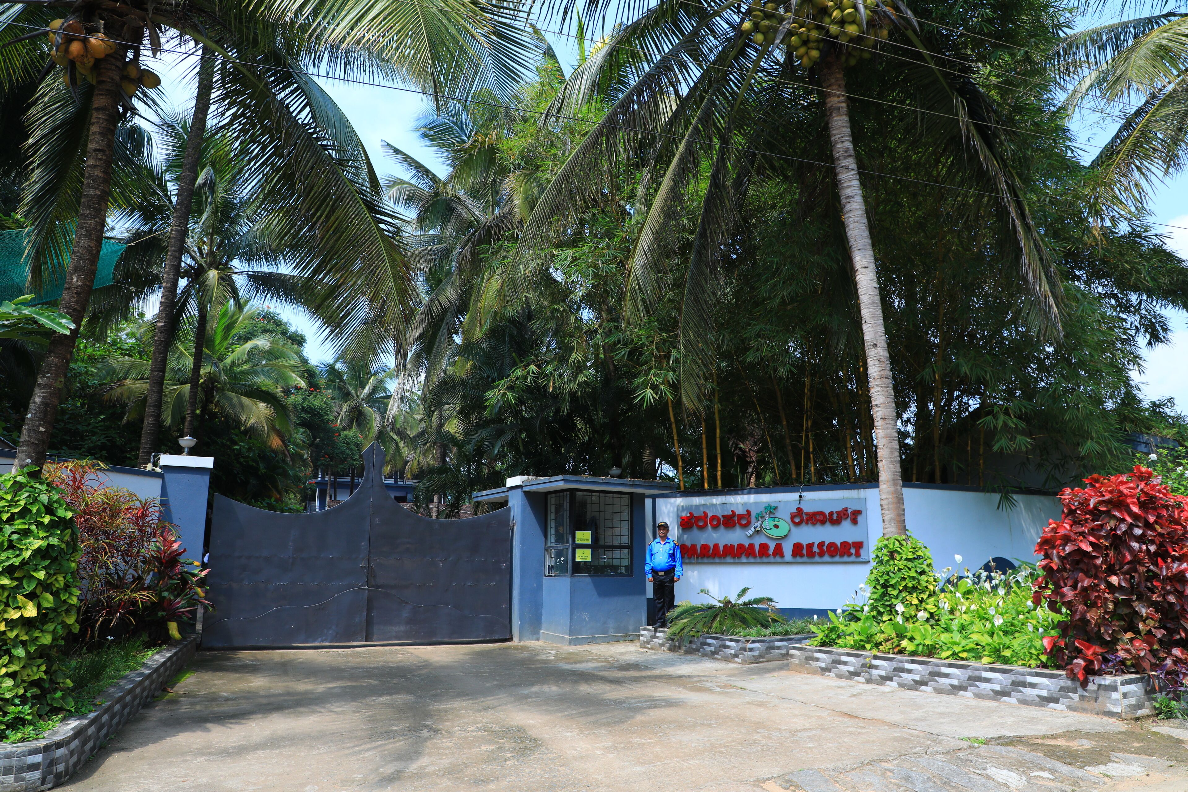 A gated entrance to a resort with a signboard, surrounded by lush greenery and palm trees.