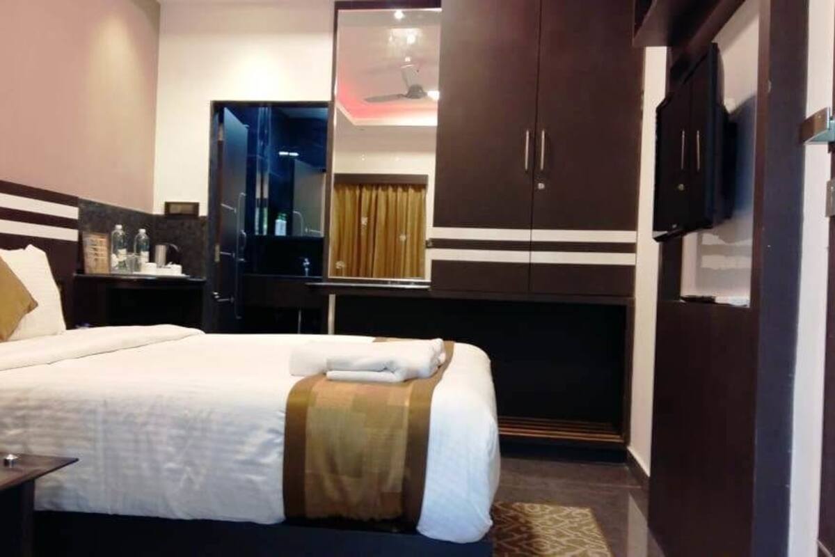 Una habitación de hotel con cama, mesita de noche, televisor, armario y espejo.