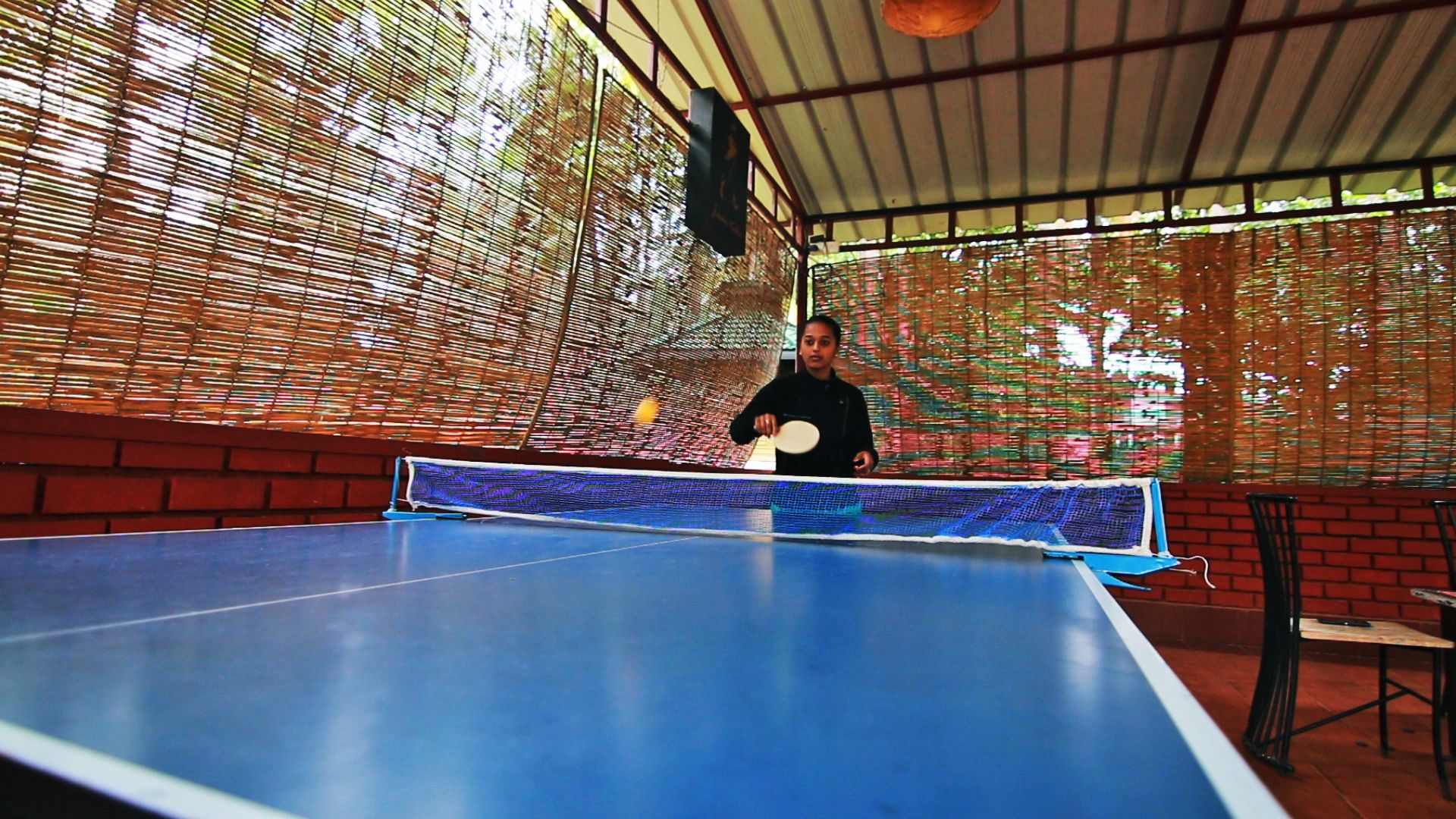 A ping pong table with a net in an indoor setting with brick walls and a metal roof.