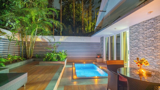 Un espace piscine extérieur moderne, doté d’une table et de chaises en verre, entouré d’une végétation luxuriante et d’un mur en pierre.