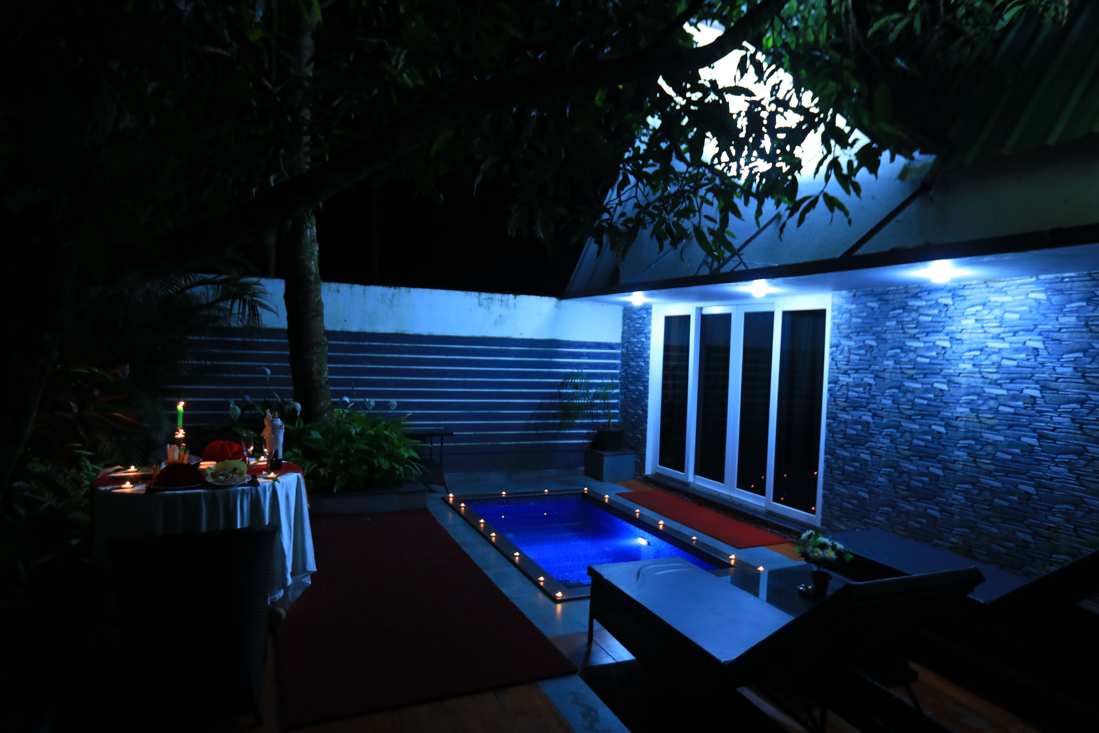 Un área de piscina al aire libre con un muro de piedra, una mesa con velas y un banco.