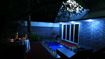 Un área de piscina al aire libre con un muro de piedra, una mesa con velas y un banco.