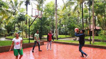 Una cancha de baloncesto cubierta con piso rojo, rodeada de palmeras y un pequeño edificio con techo rojo.