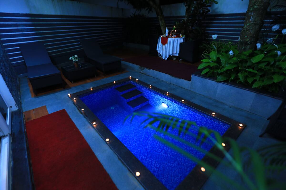 Una piscina con una alfombra roja que la conduce, rodeada de sillones de descanso y una mesa con velas.