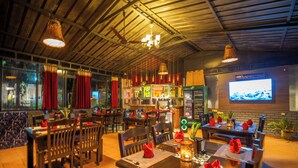 Un restaurant avec des tables et des chaises en bois, un coin bar et un écran de télévision fixé au mur.
