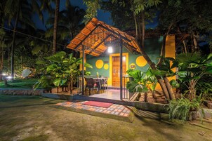 Un espacio al aire libre acogedor con una mesa y sillas, rodeado de exuberante vegetación tropical y un mural colorido en el edificio.