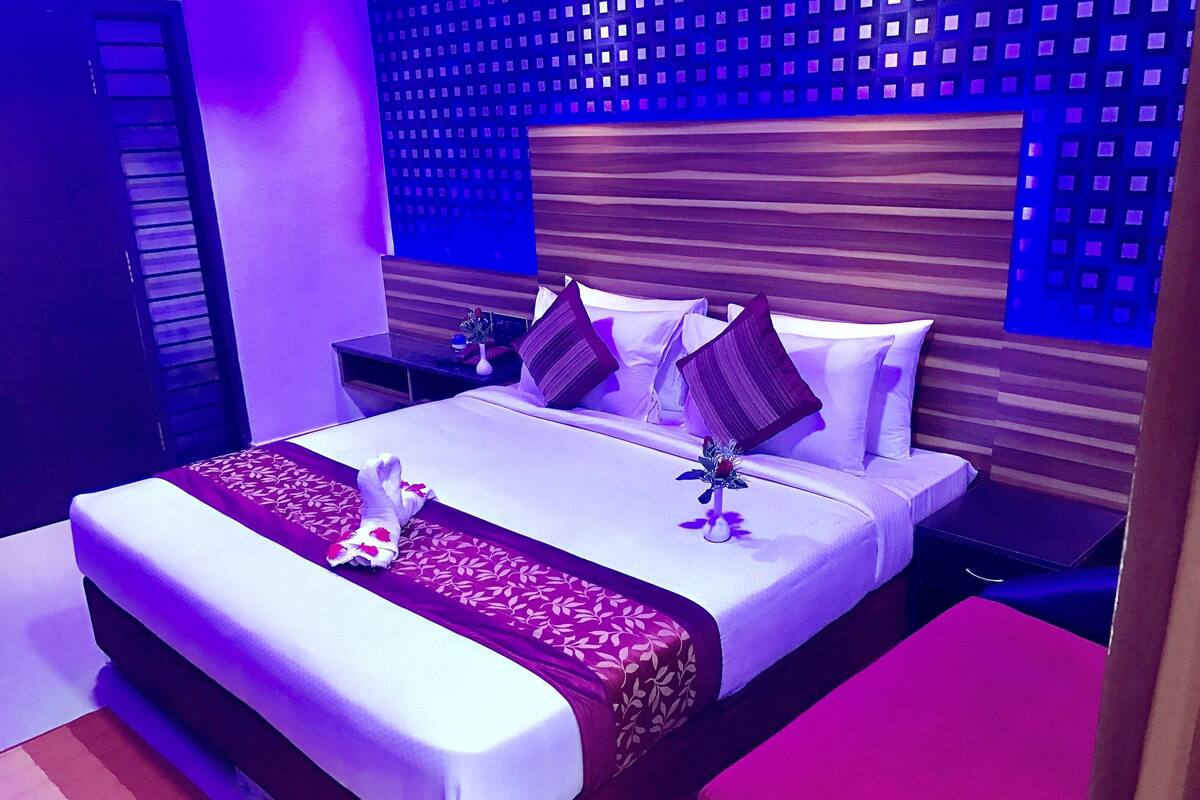 Habitación de hotel con una cama grande, una mesita de noche, una pequeña mesa y una pared con diseño decorativo.