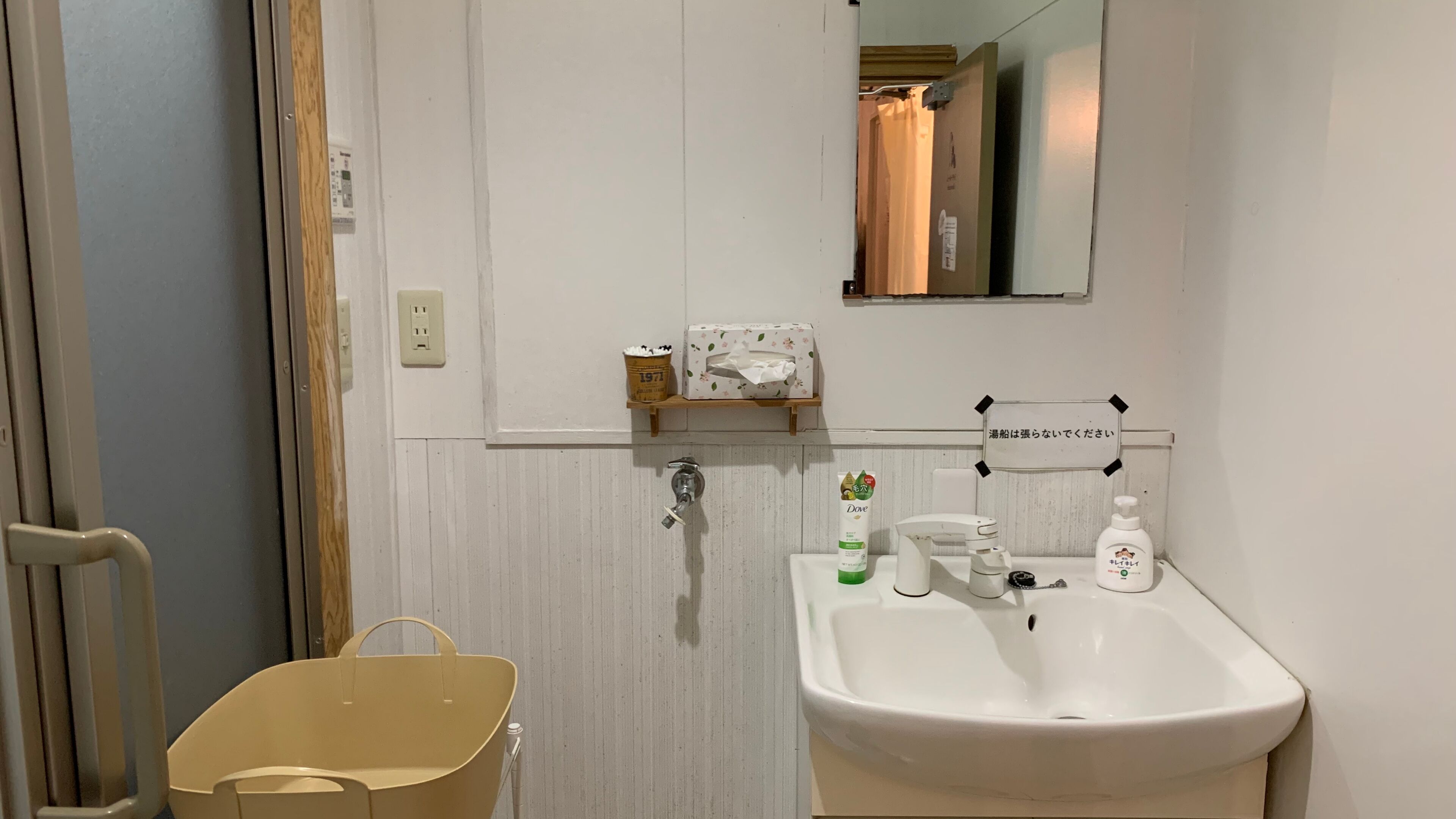 A bathroom with a white sink, a mirror, a towel dispenser, and a small shelf with toiletries.