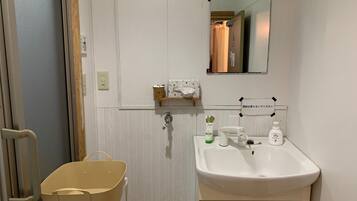 A bathroom with a white sink, a mirror, a towel dispenser, and a small shelf with toiletries.