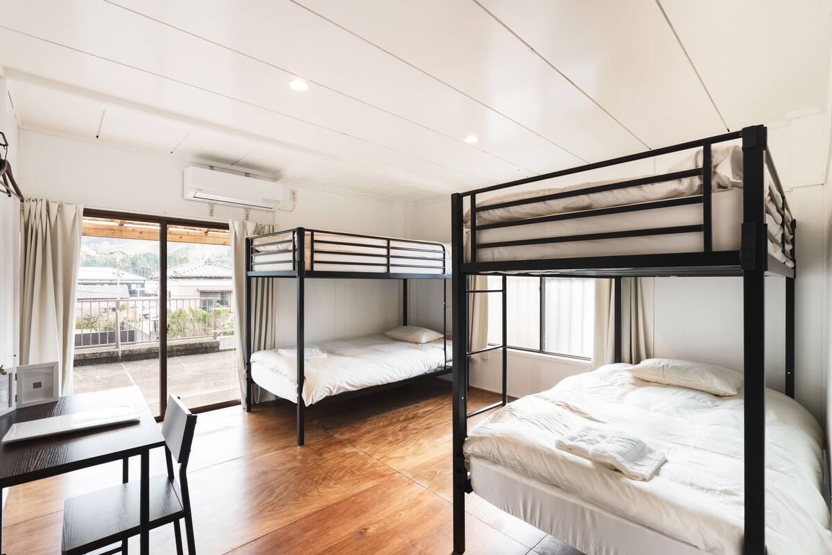 A dormitory room with bunk beds, a desk, and a laptop.