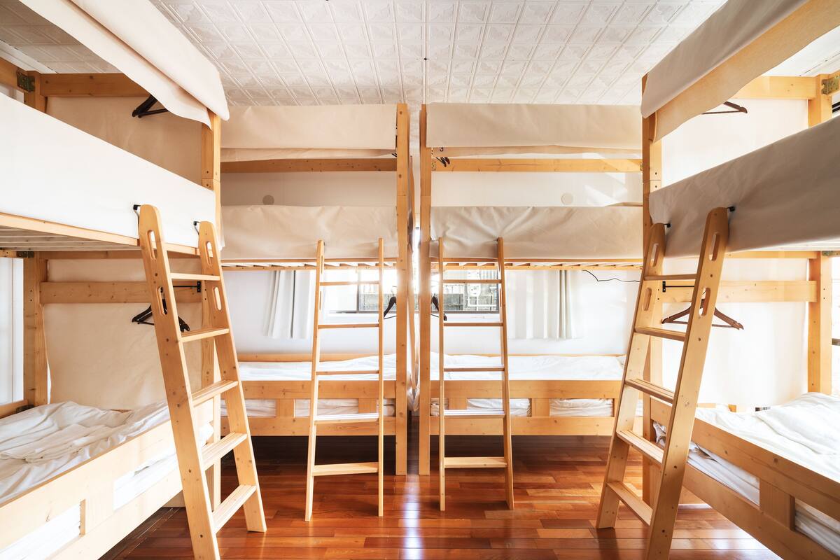 A room with four bunk beds, wooden ladders, and a window with curtains.