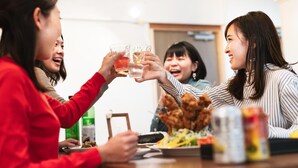 Un groupe de personnes trinquant avec des boissons autour d’une table où se trouvent de la nourriture et des condiments.