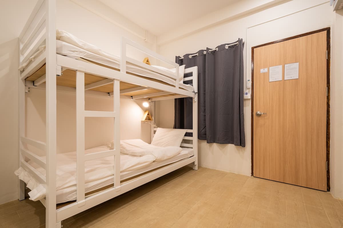 A bunk bed room with a wooden door, a nightstand with a lamp, and a curtain.