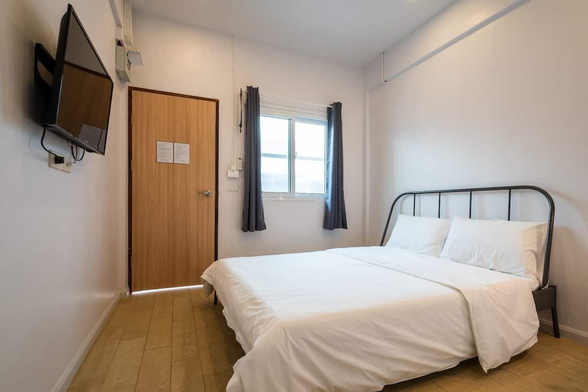 A bedroom with a bed, a TV mounted on the wall, a window with curtains, and a door with a sign.