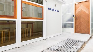 A building with a white exterior, a wooden door, and a sign that reads "MORNINGS". - Morn-Ing Hostel (Bangkok)