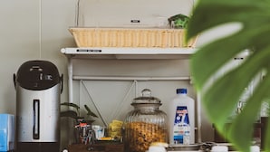 A kitchen counter with a coffee maker, a basket, and various kitchen items. - Morn-Ing Hostel (Bangkok)