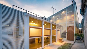 A modern building with large glass windows, a wooden door, and a small outdoor seating area with stools. - Morn-Ing Hostel (Bangkok)
