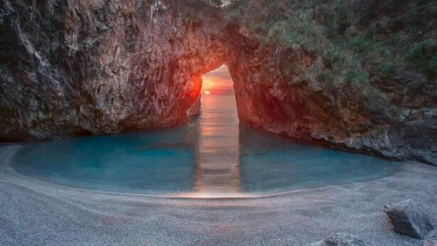 Formación rocosa natural con un canal de agua clara que desemboca en una playa.