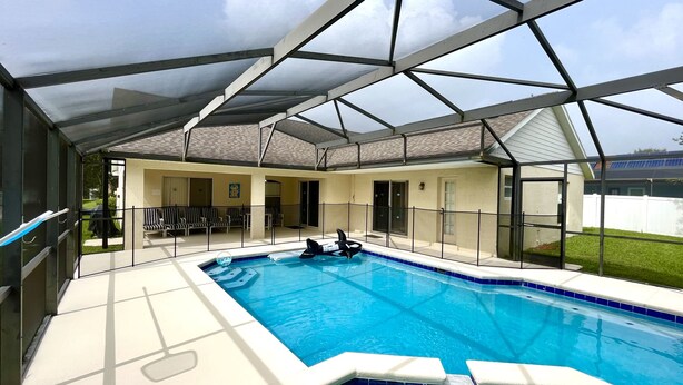 Una piscina interior con techo de cristal, sillas de descanso y vistas al jardín trasero.