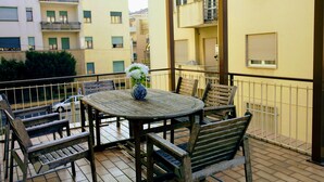 A balcony with a round wooden table and chairs, a vase with flowers, and a view of adjacent buildings. - Rosa Garden B&B (Mestre)