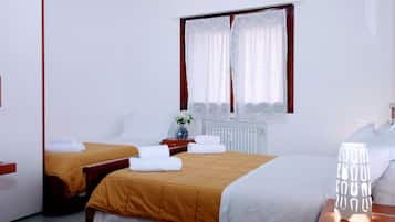 A hotel room with two beds, a window with curtains, a bedside table with a vase, and a lamp.