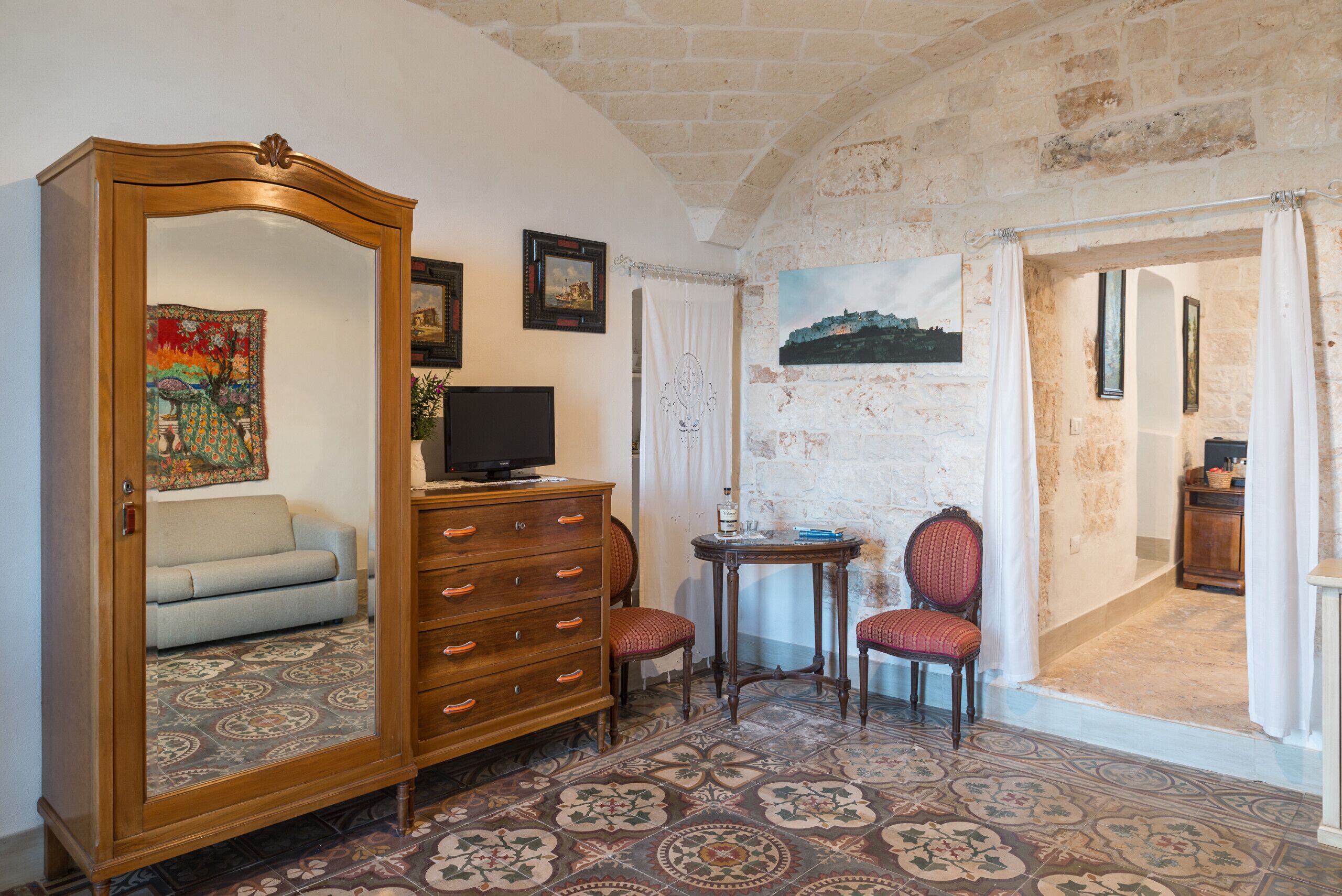 A room with a large mirror, a wooden dresser, a television, and a small table with a chair.