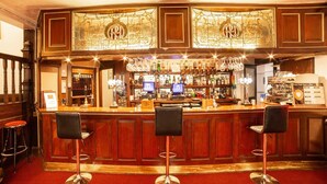 A bar area with a wooden counter, bar stools, and a decorative stained glass window above. - Royal Hotel (Kettering)