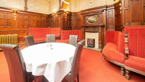A formal dining room with a round table, red upholstered chairs, a fireplace, and wooden paneling. - Royal Hotel (Kettering)