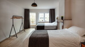 A modern hotel room with a large bed, a smaller bed, a wardrobe, a hanging light fixture, and a view of buildings through the window. - Big Baron Holiday Home Bruges - Free parking (Brugge)