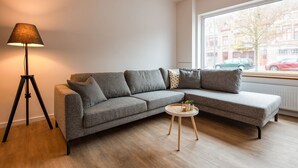 A modern living room with a grey sectional sofa, a floor lamp, and a small round table. - Big Baron Holiday Home Bruges - Free parking (Brugge)