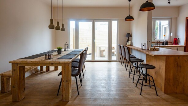 A spacious kitchen with a wooden dining table, bar stools, pendant lights, and a large window. - Big Baron Holiday Home Bruges - Free parking (Brugge)