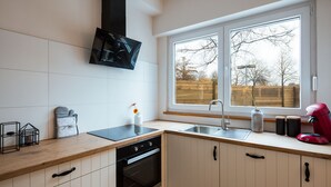 A modern kitchen with a built-in oven, a stovetop, a sink, and a window with a view of a wooden deck. - Big Baron Holiday Home Bruges - Free parking (Brugge)