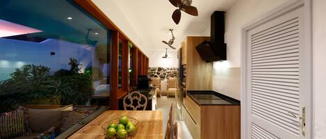 A modern kitchen with wooden cabinets, a dining area with a wooden table, and a large window overlooking a garden.