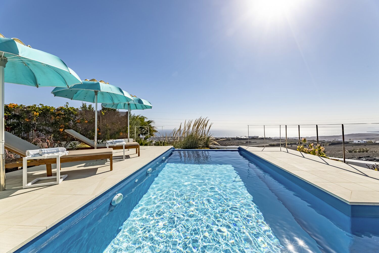 Une piscine avec des chaises longues et des parasols, un ciel dégagé et une vue sur le paysage.