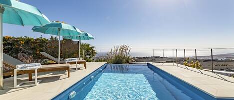 Une piscine avec des chaises longues et des parasols, un ciel dégagé et une vue sur le paysage.