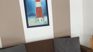 En brun sofa med to grå puder og et indrammet maleri af et fyrtårn på væggen.
