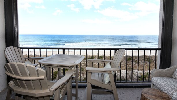 Een balkon met twee Adirondack-stoelen en een kleine tafel, met uitzicht op een strand en de oceaan.