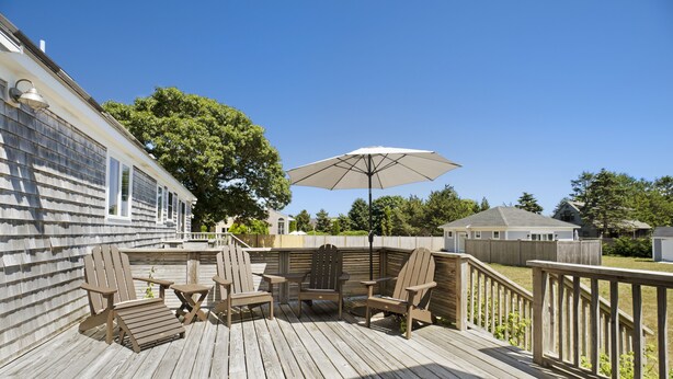 Eine Holzterrasse mit Adirondack-Stühlen und einem Tisch, umgeben von einer Holzbrüstung.